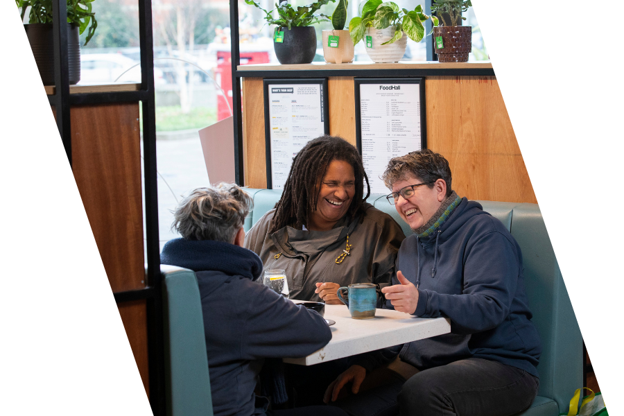 Three people laughing drinking a hot drink at a table
