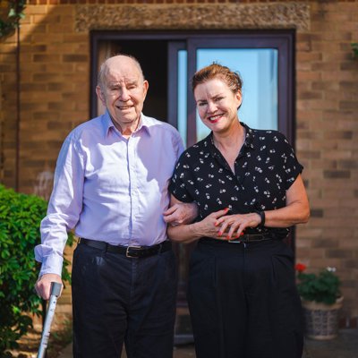 A younger woman helping an elderly man navigate an outdoor setting. 