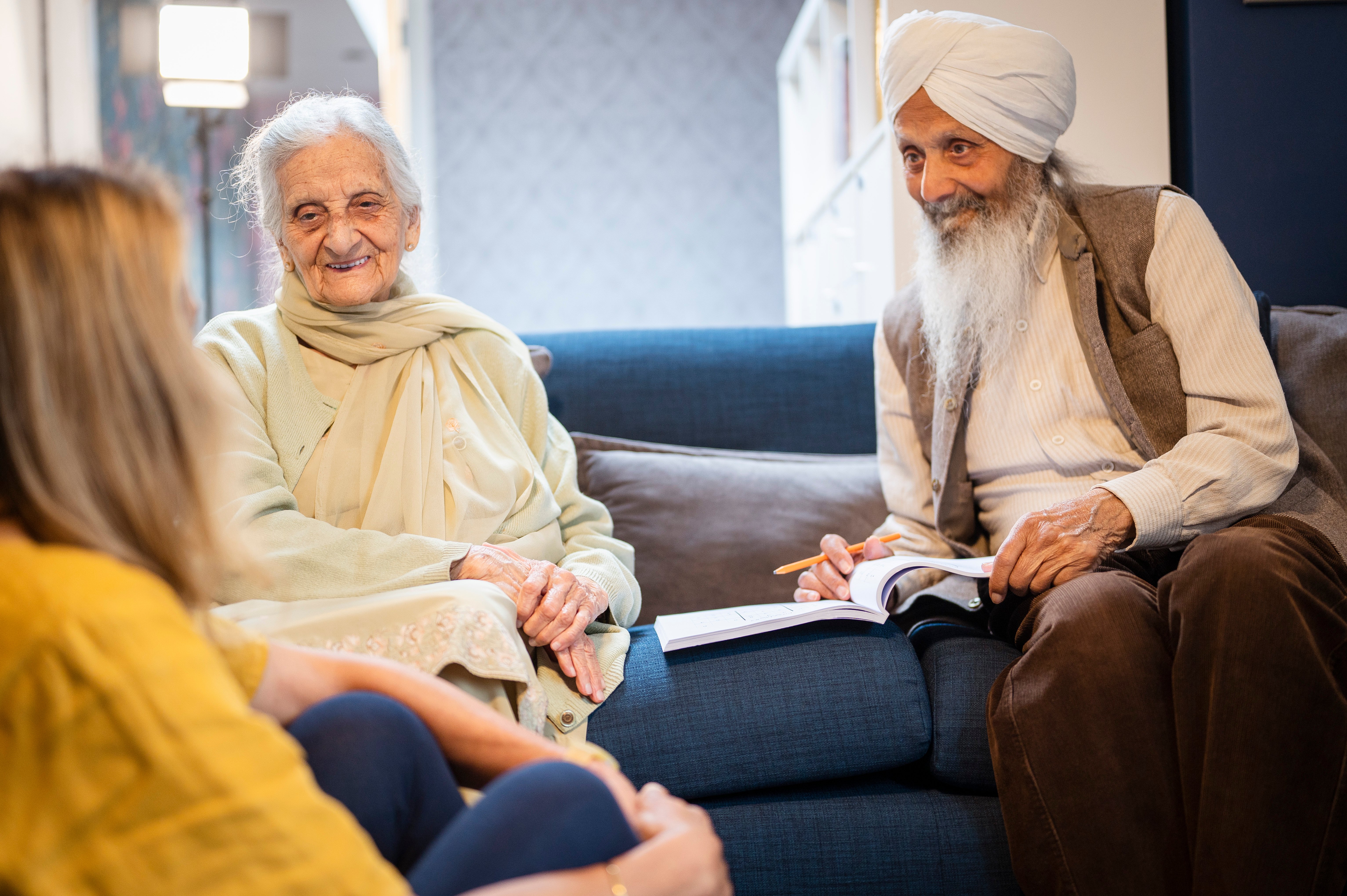 An elderly man and woman converse on a couch with a younger woman, creating a warm and engaging atmosphere.
