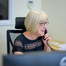 A woman wearing glasses is engaged in a conversation on her phone, appearing focused and attentive.