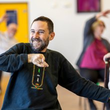 A cheerful man engaging in chair based exercise in a group setting.