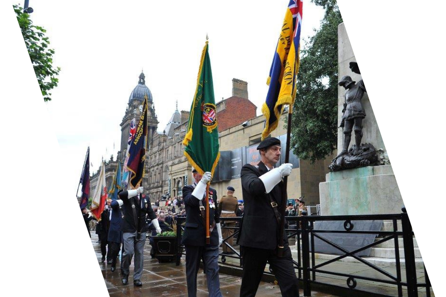 Veterans and families participating in a ceremony, carrying flags, in front of a war memorial